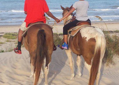 Two Boys riding horses on a sunny beach with joining hands