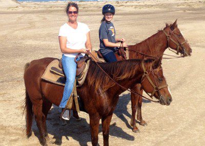 2 girls horseback riding on the beach.