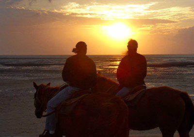 Two girls riding horses on a beach during sunset