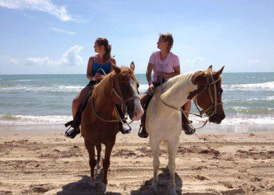 Two people riding horses on a sunny beach.