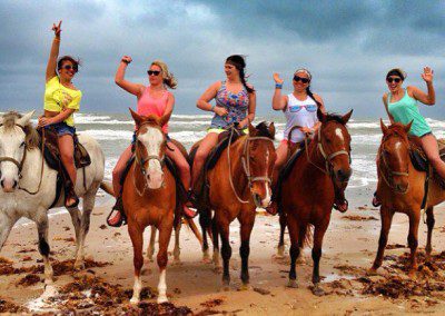 Group of people horseback riding on the beach.